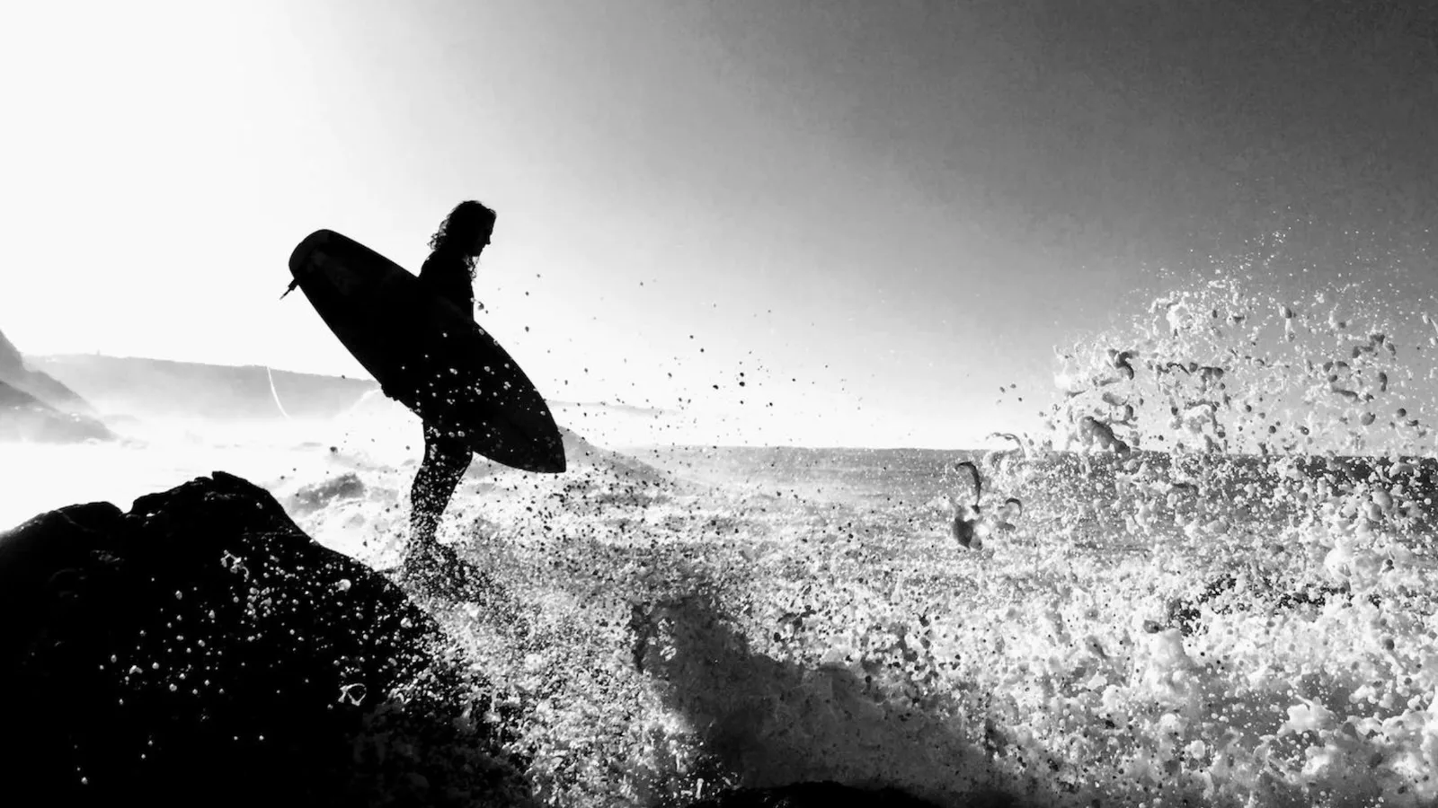 A surfer beside a wave-swept coastline
